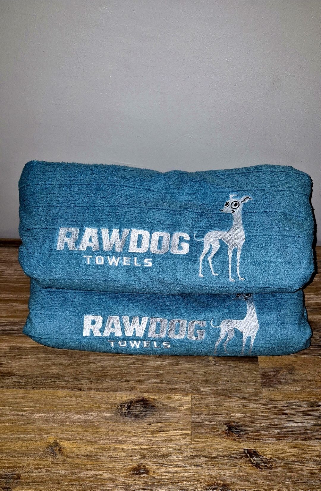 Two Rawdog towels folded in a stack, showing the embroidered wordmark and whippet.