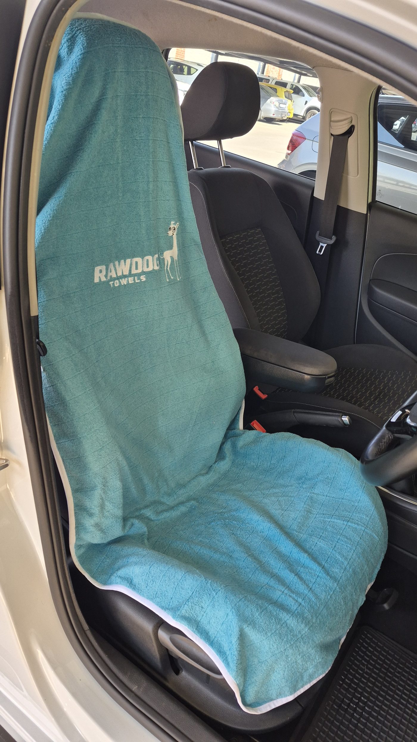 A Rawdog towel fitted over a driver's seat, showing the embroidered wordmark and whippet on the backrest.