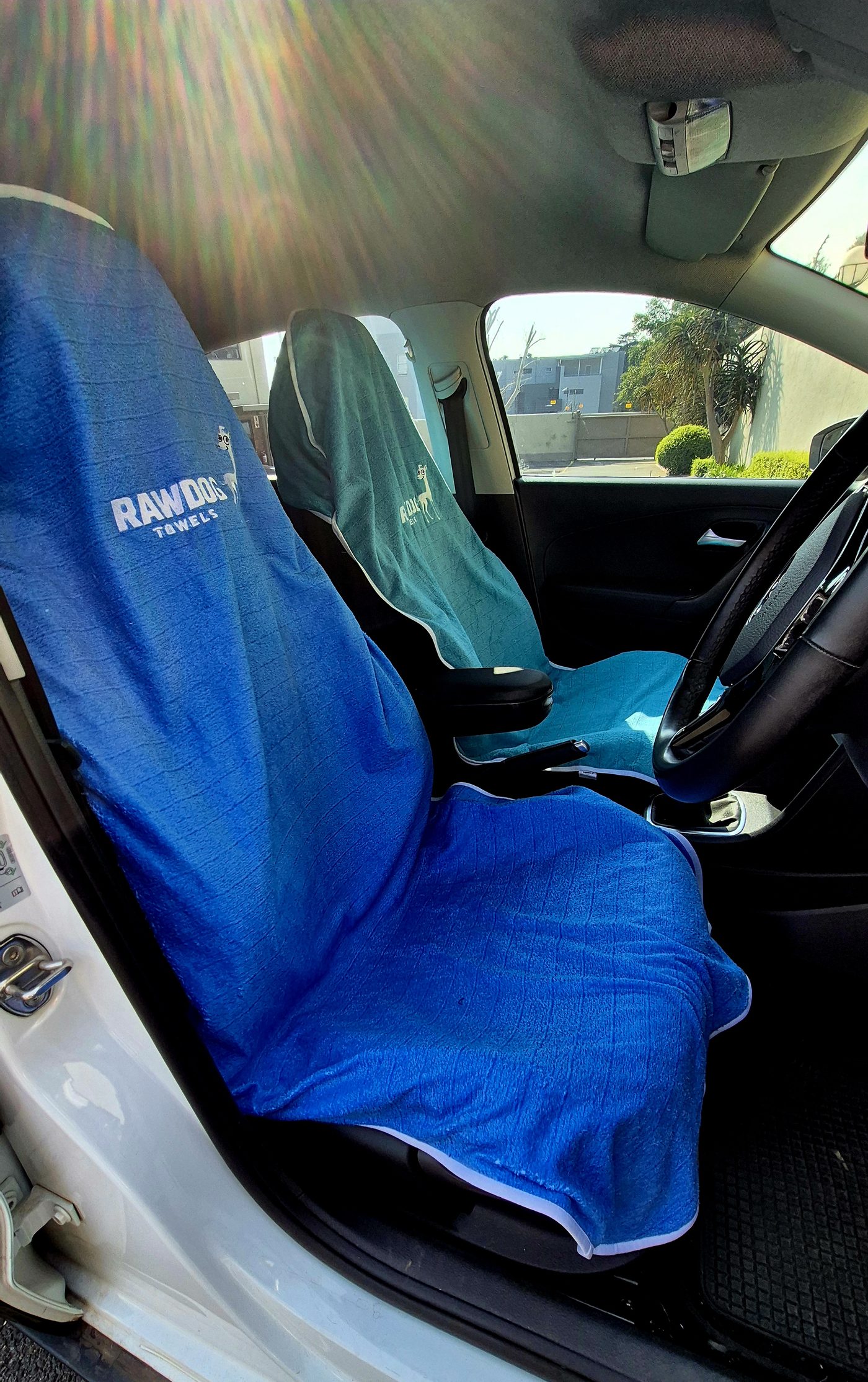 Both front seats of a car fitted with Rawdog towels, seen from the open passenger door.