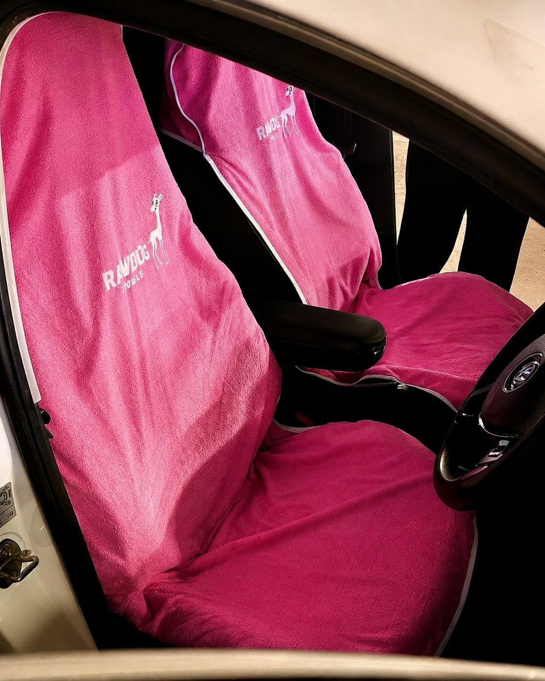 Both front seats of a car fitted with pink Rawdog towels, seen through an open car door.